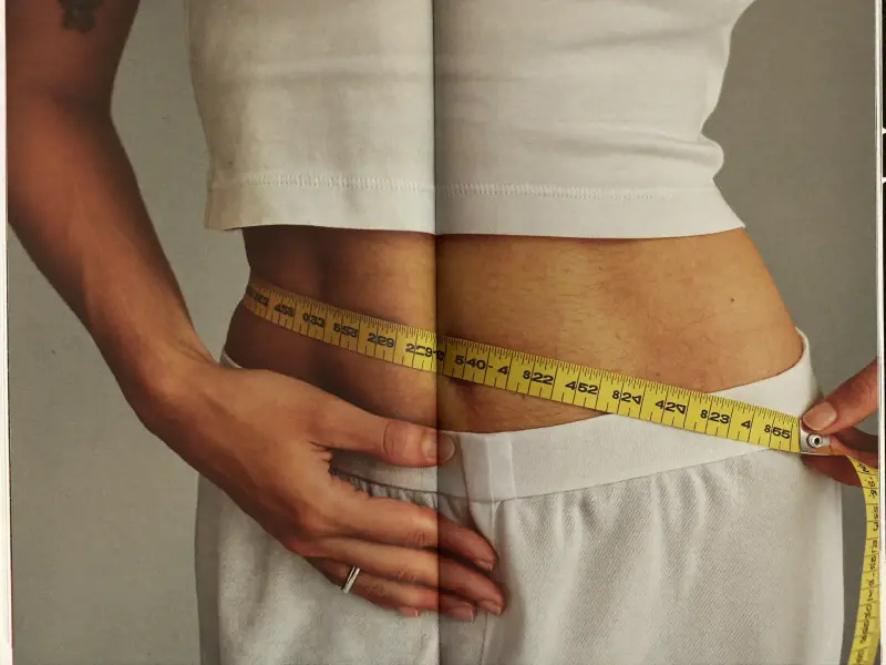 A person measuring their waist with a tape measure.