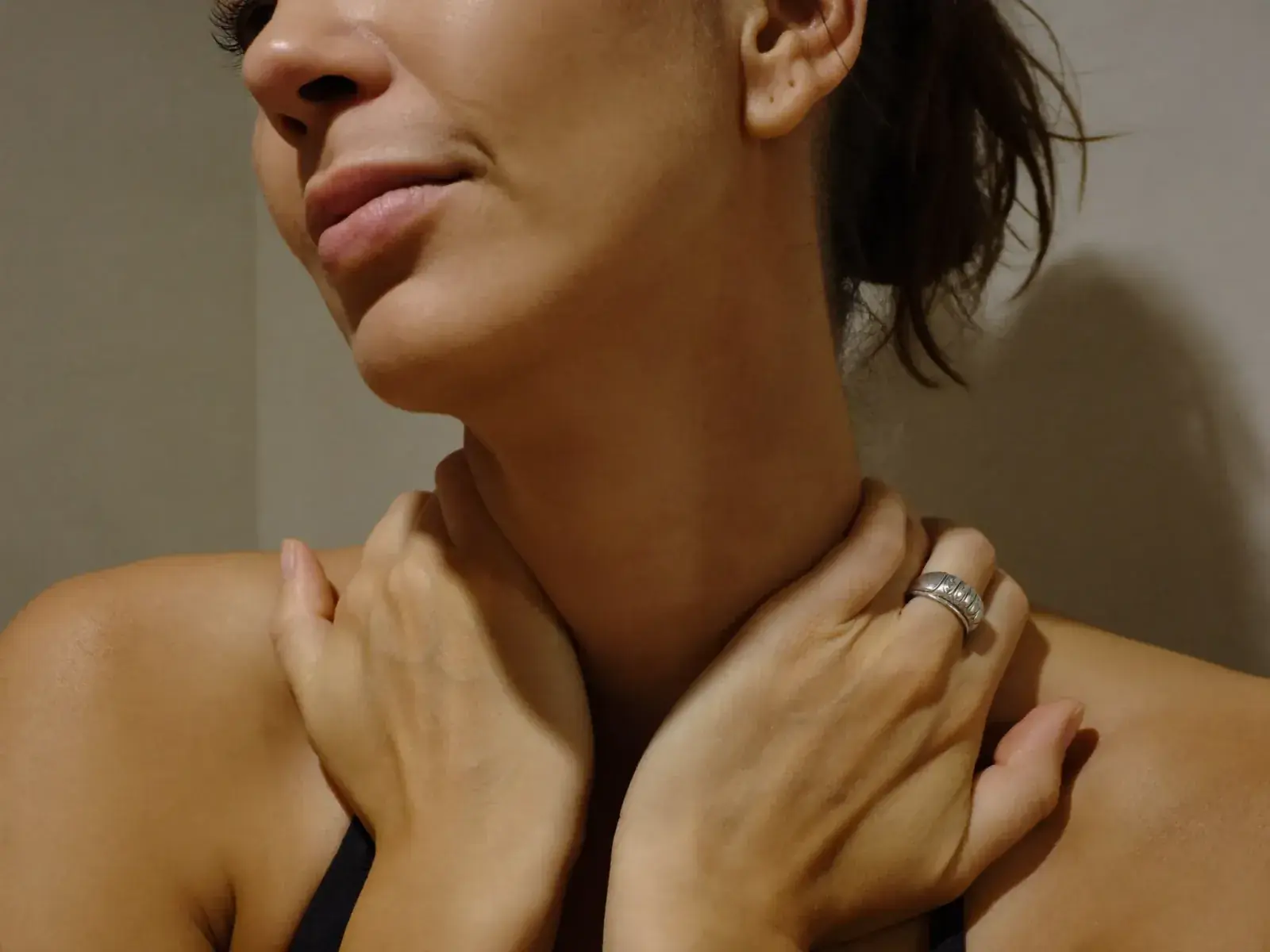 A woman gently resting her fingers on the front of her neck.