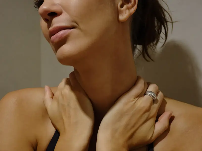 A woman gently resting her fingers on the front of her neck.
