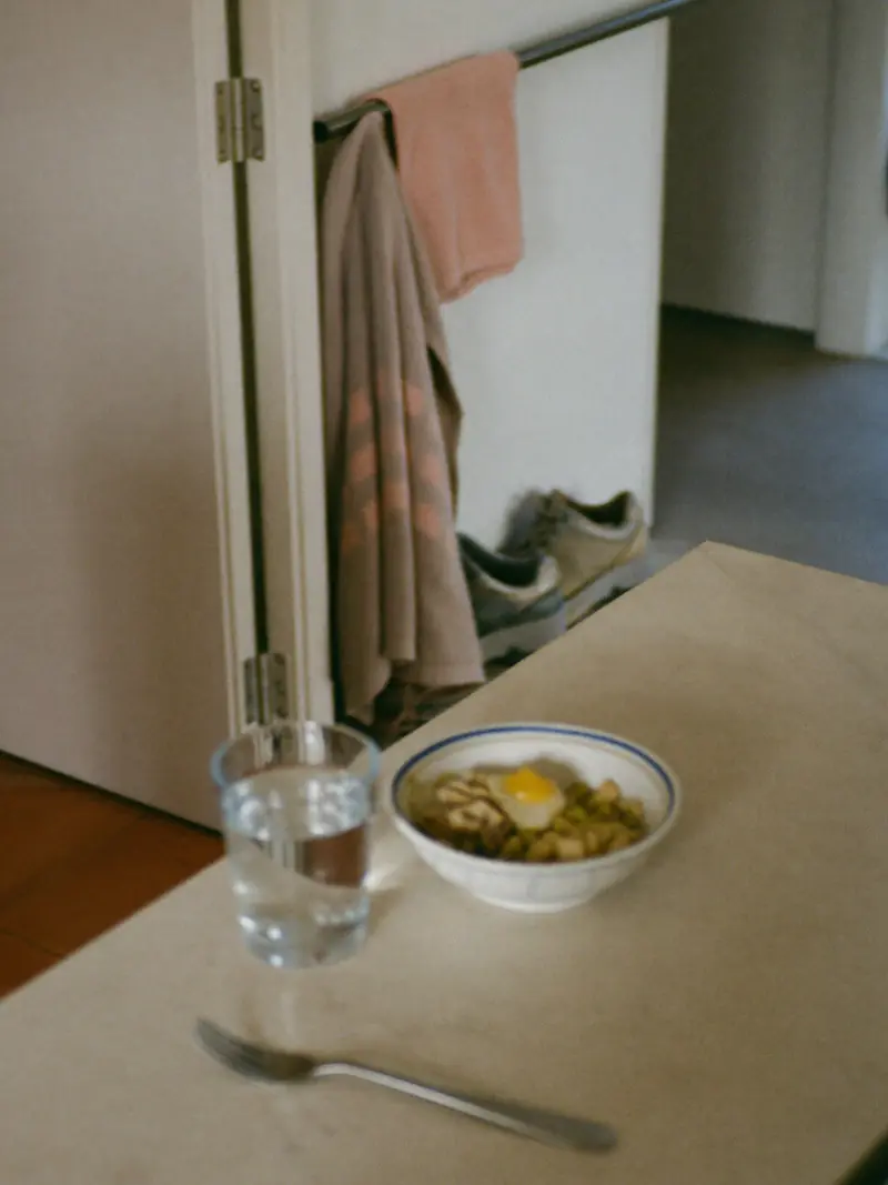 Morning light across a kitchen counter: a glass of water, a bowl of home-cooked food, walking shoes by the door.