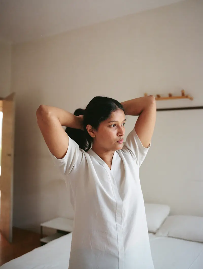 A woman tying her hair back by a window in morning light.